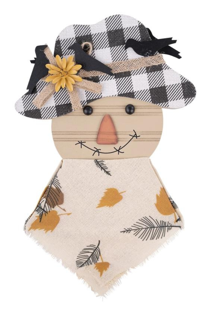 A wooden scarecrow topper featuring a black and white buffalo plaid hat adorned with a yellow flower, burlap ribbon, and black bird cutouts. The scarecrow's face is light wood with black button eyes, a triangular orange nose, and a drawn black smile with stitches. A cream-colored fabric body with printed autumn leaves and feather designs hangs below the head.