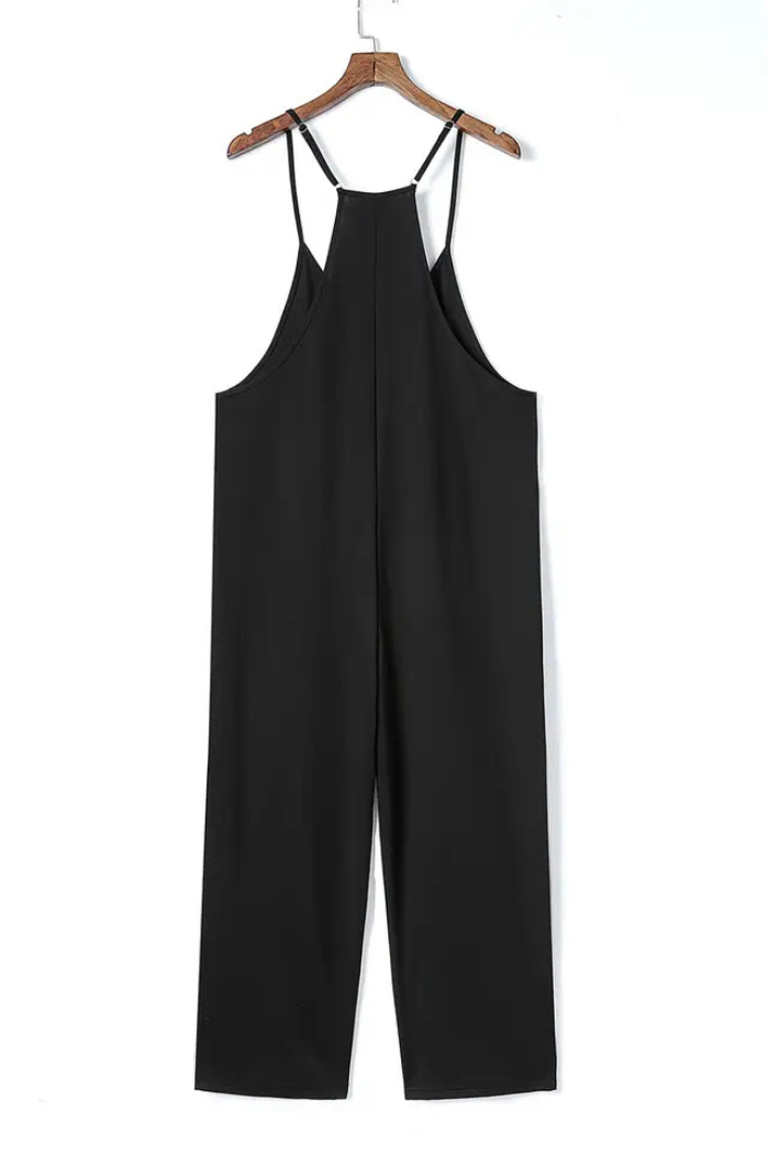 A black spaghetti strap wide-leg jumpsuit hanging on a hanger. The jumpsuit has a V-neck and two straps. The legs are wide and loose. The material looks smooth and comfortable. This is likely a casual, summer-style outfit.