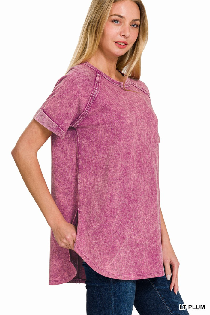 A woman wearing a light plum-colored, acid-wash French terry short-sleeve pullover with cuffed sleeves, a round hemline, and side slits, standing against a white background.