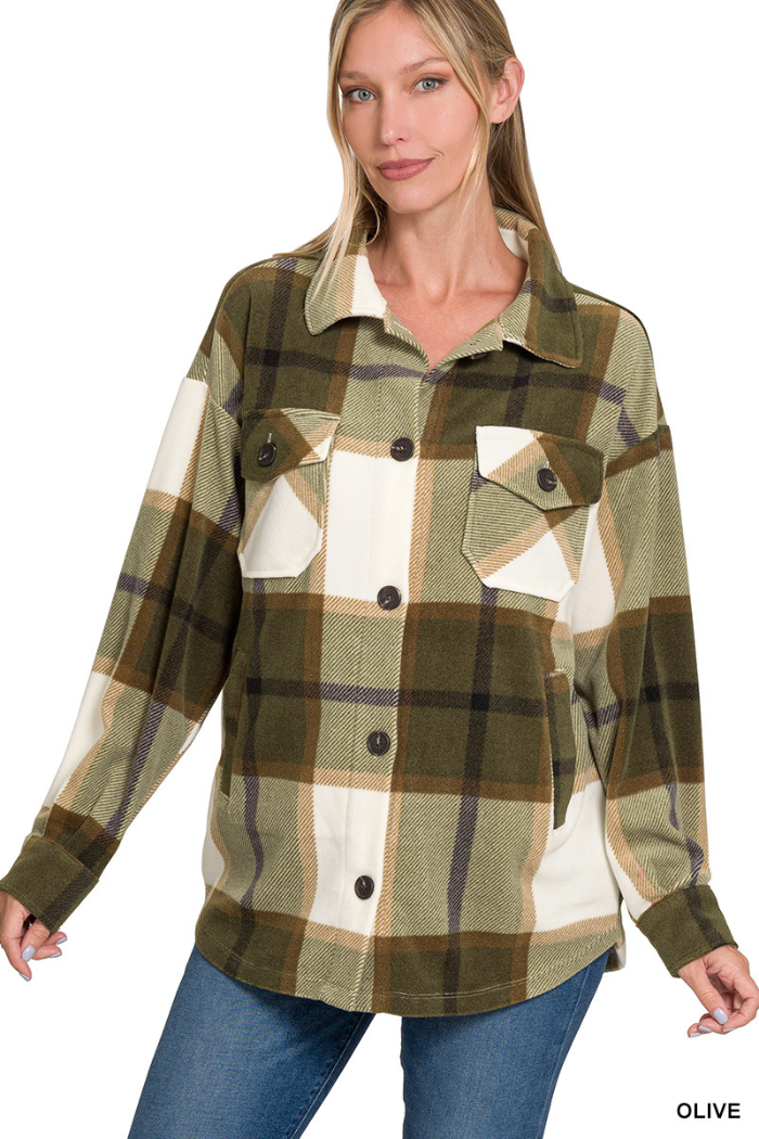 A woman with blonde hair wearing an oversized olive green, cream, and brown plaid shacket with front pockets and buttons.