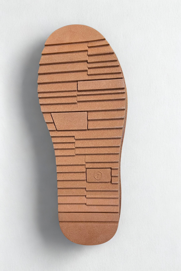 A close-up of the brown, textured rubber sole of a shoe. The sole has a chunky, geometric pattern of horizontal and vertical rectangular blocks. The number "7" is visible in a small circular indentation near the heel.