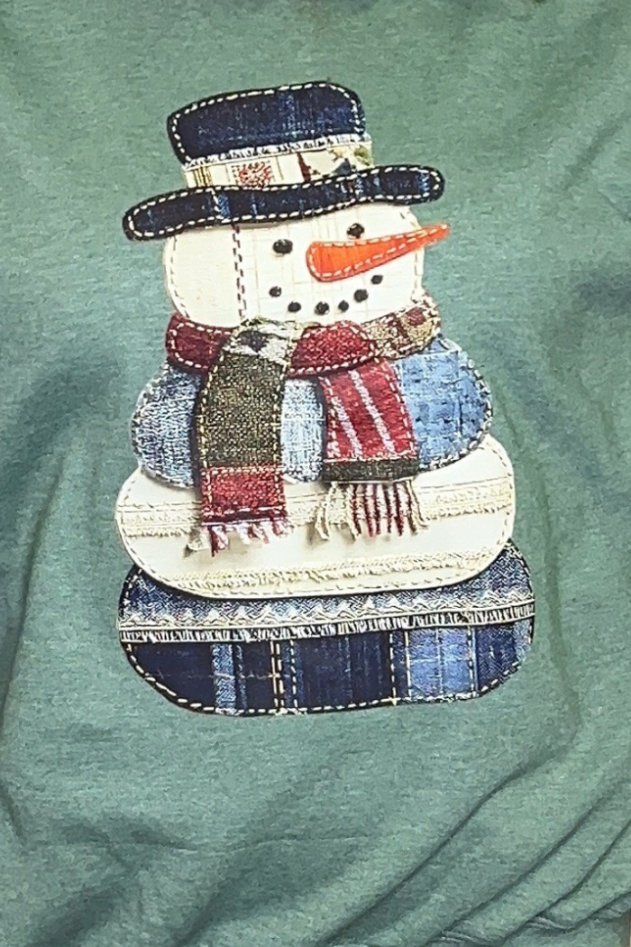 The Snowman Patchwork Holiday Sweatshirt features a fabric snowman applique with a plaid scarf, hat, and patches, button eyes, and a carrot nose on a green backgroundβperfect for cozy holiday or farmhouse Christmas style.