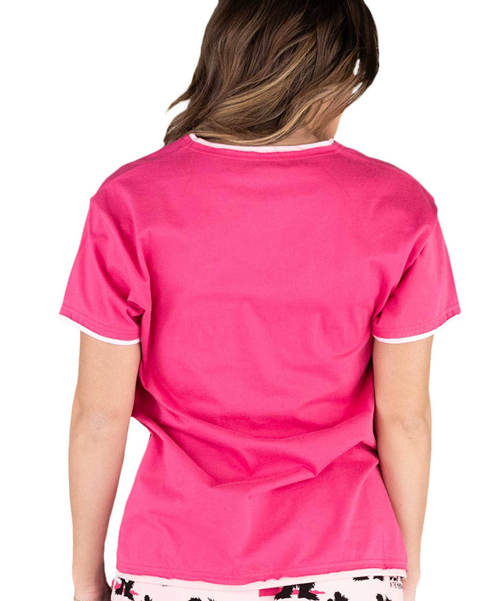 A person with medium-length brown hair is facing away from the camera, wearing a Dog Mom, Cat Nap & More Pajama Top in bright pink with white trim and novelty print shorts. The background is white.