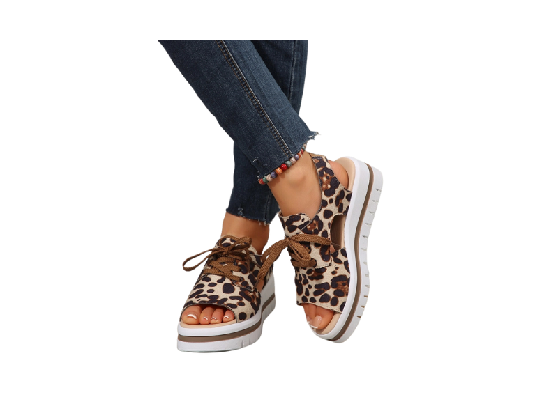 Women's leopard print wedge sandals. These sandals feature a platform sole, brown laces, and an ankle strap. The leopard print is a classic pattern that has been trending in fashion for many years. It's a versatile print that can be dressed up or down, making it a popular choice for both casual and more formal occasions. The leopard print consists of black spots with brown centers, which distinguishes it from cheetah print, which has solid black spots. 