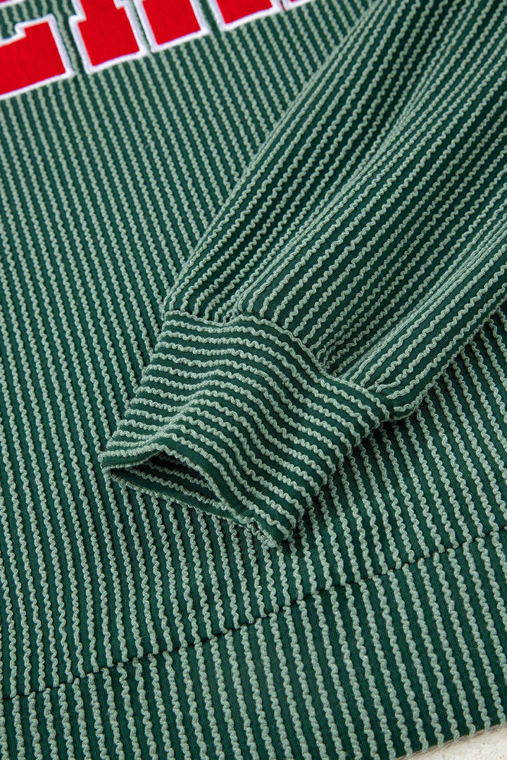 Close-up of the ribbed green fabric with white and dark green horizontal stripes, highlighting the cuff and hem of the Merry Graphic Top—a long-sleeve festive piece with red and white text partially visible at the top, perfect for holiday gatherings or cozy winter wear.