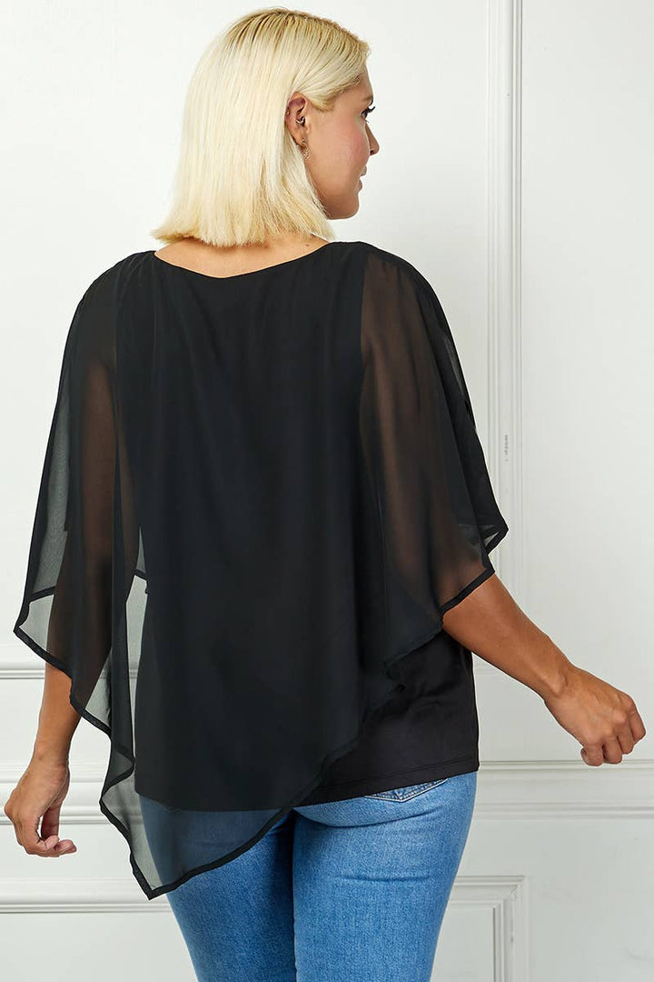 A woman with blonde hair, seen from the back, wears the Plus Blooming Poncho Blouse—a black sheer overlay with flowy sleeves—over blue jeans. She stands against a light-colored wall.