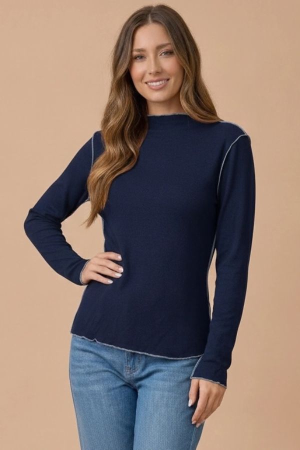 Woman wearing a navy blue Frilled Mock Neck Hacci top with exposed light-colored stitching at the seams and edges.