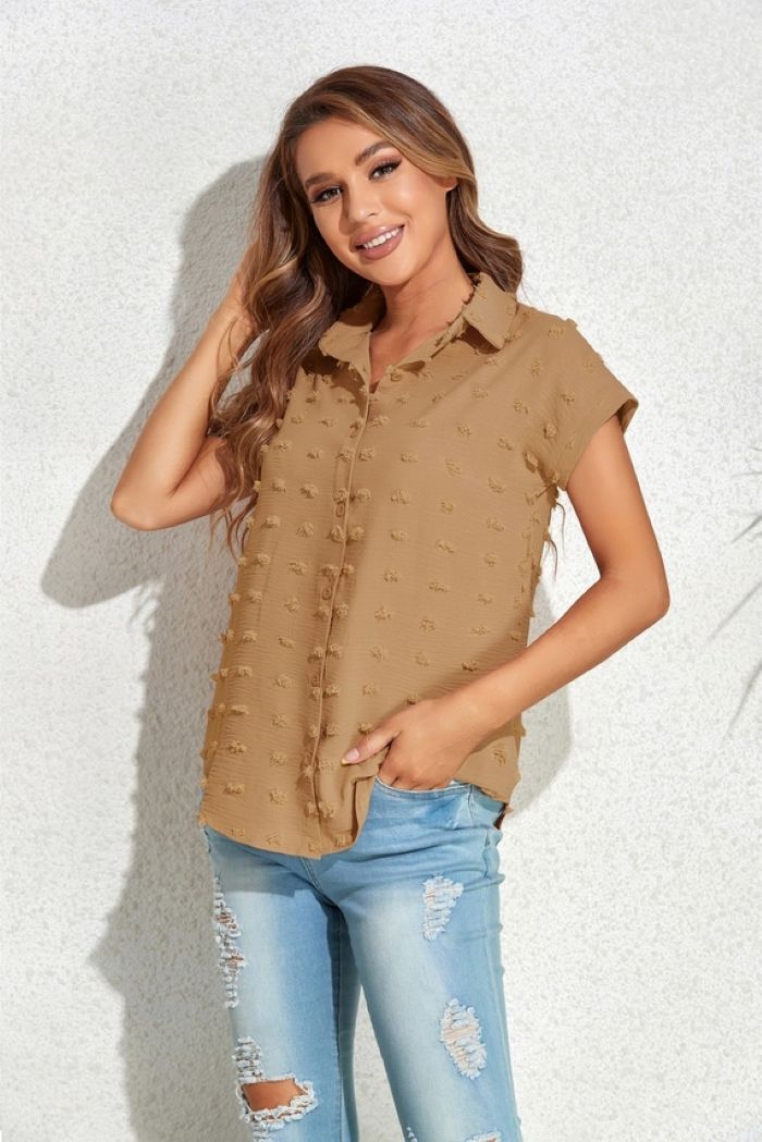 A woman with long brown hair smiles, wearing a Textured Button Blouse that pairs perfectly with ripped light blue jeans. She stands against a light wall, one hand in her pocket and the other touching her hair.