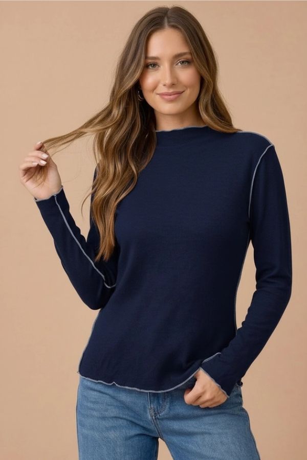 A woman wearing a navy blue Frilled Mock Neck Hacci top with exposed light-colored stitching and blue jeans.