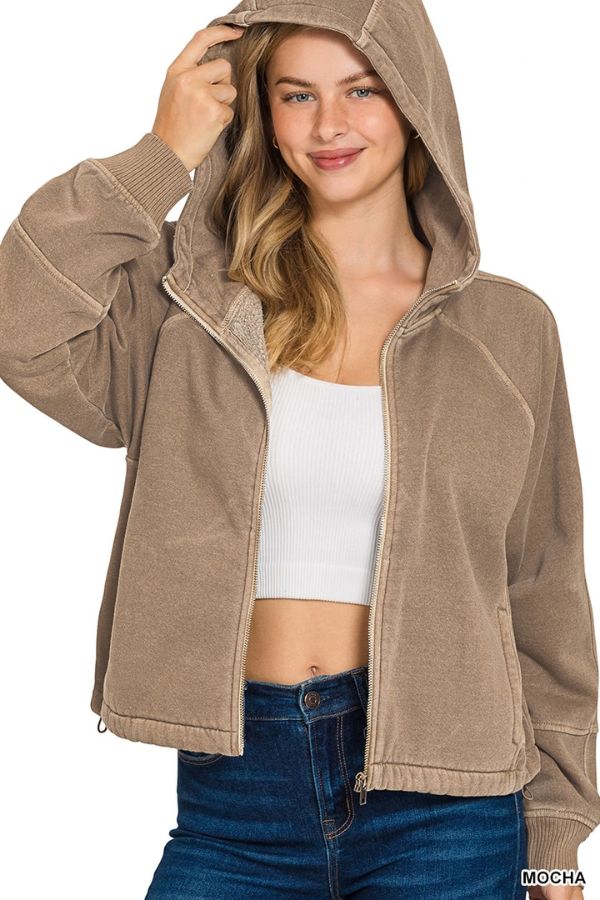 Woman wears the Pigment Dye Zip Up Hoodie, a brown zip-up fleece with adjustable hem, over a white crop top and blue jeans, smiling and holding the hood up for a relaxed look.