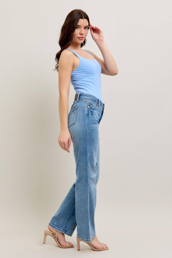 The image shows a woman wearing Judy Blue Mid Rise Tummy Control Vintage Wash Straight Leg Jeans paired with a light blue tank top and nude heels. 