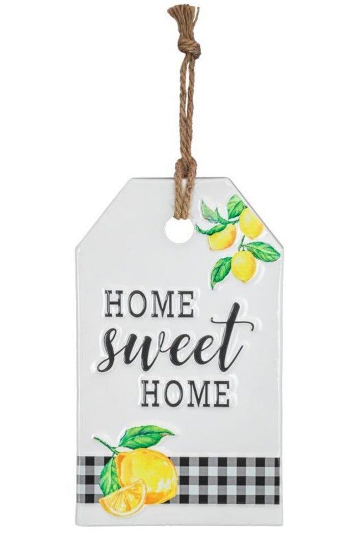 A tag-shaped home decor item with the text "HOME sweet HOME" printed on it, adorned with lemon illustrations and a black and white checkered pattern at the bottom. 