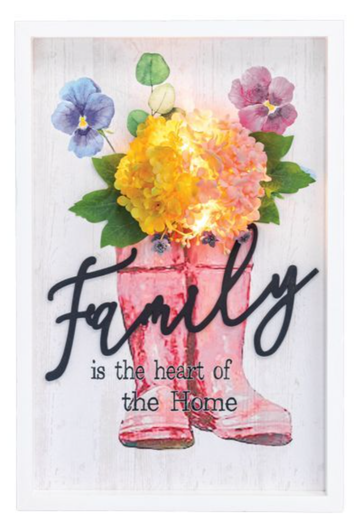 Decorative sign with pink boots, flowers, and 'Family is the heart of the home' text.