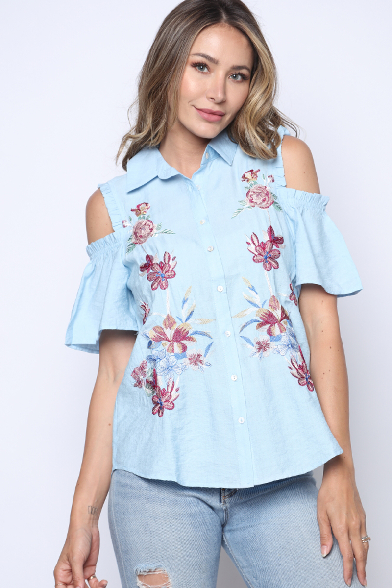 Woman wearing a light blue blouse with floral embroidery on a white background