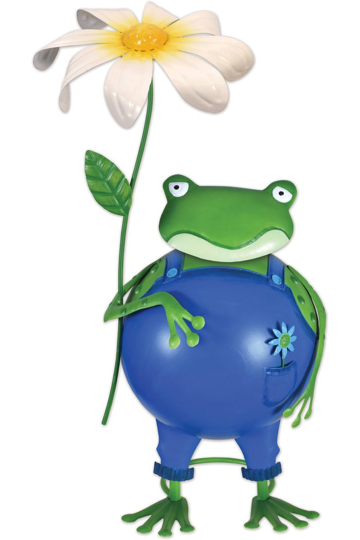 Decorative metal garden sculpture of a green frog with a white flower. The frog is wearing blue overalls with a small blue flower on the pocket. The frog has a somewhat grumpy expression. The flower is held by the frog's right hand.