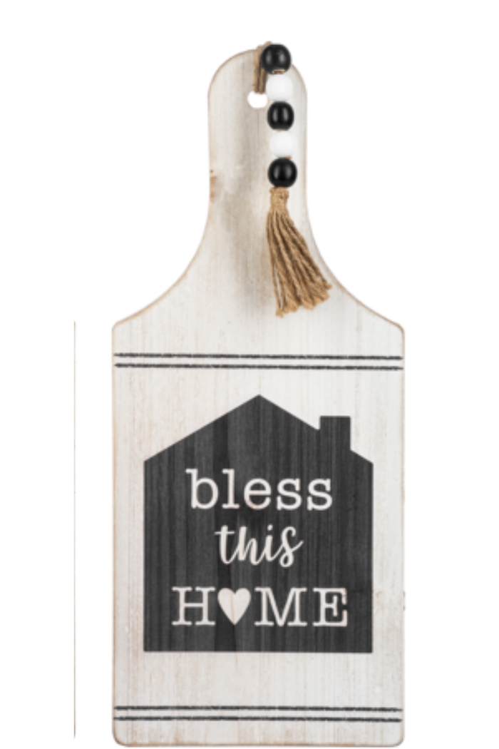 Wooden cutting board with 'bless this home' text and tassel on a white background