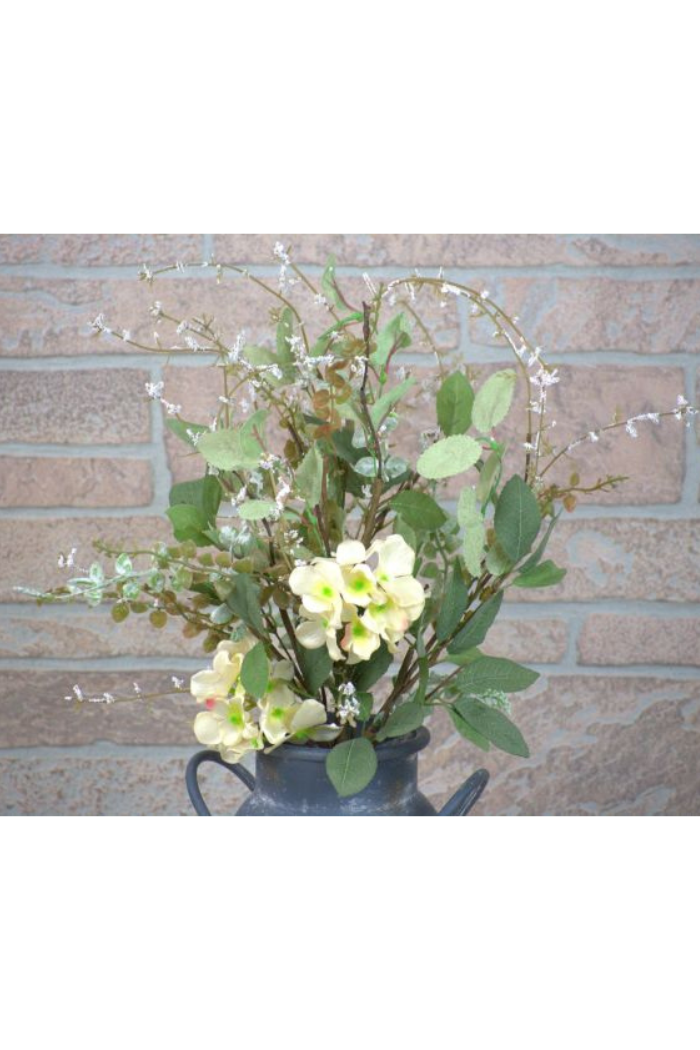 Artificial flower arrangement with green leaves and white flowers in a pot against a brick wall.