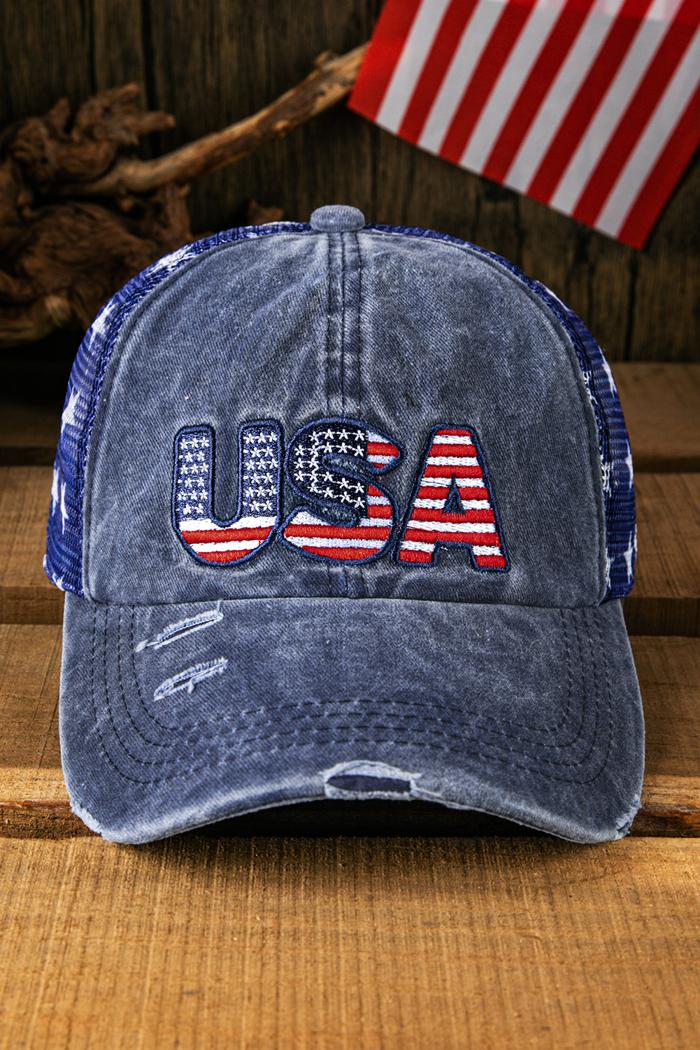 Blue denim baseball cap with a mesh back, featuring the letters "USA" embroidered on the front in a design that incorporates the American flag's stars and stripes. The cap has a distressed, vintage look with frayed edges and faded color