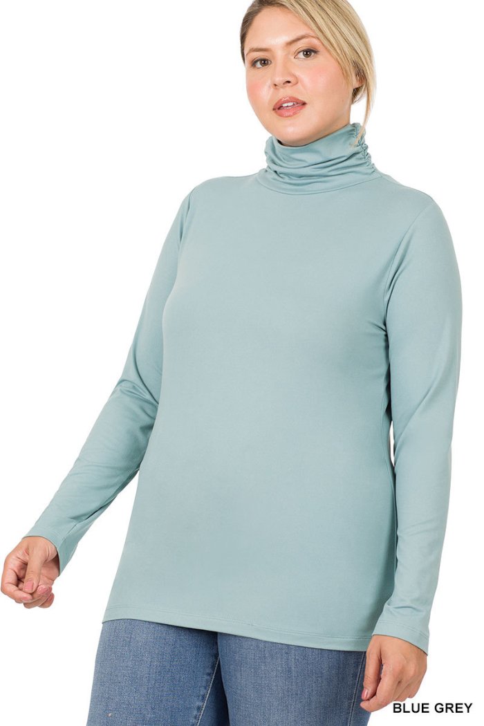 A woman wearing a long-sleeved, light blue-grey mock turtleneck top, with the text "BLUE GREY" in the bottom right corner. 
