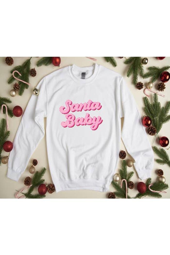 White sweatshirt with 'Santa Baby' text surrounded by Christmas decorations on a beige background