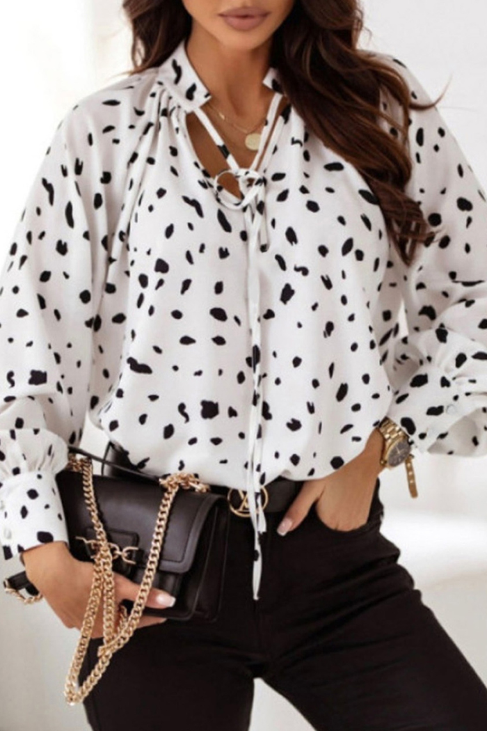 Woman wearing a white blouse with black polka dots and holding a black handbag.