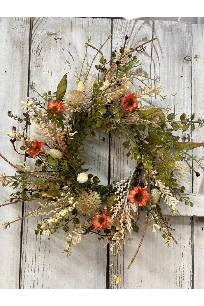 Prairie Fields Candle Ring, featuring a circular arrangement of artificial foliage and flowers. It includes green leaves, sprigs of dried-looking plants, and small orange flowers resembling dahlias.