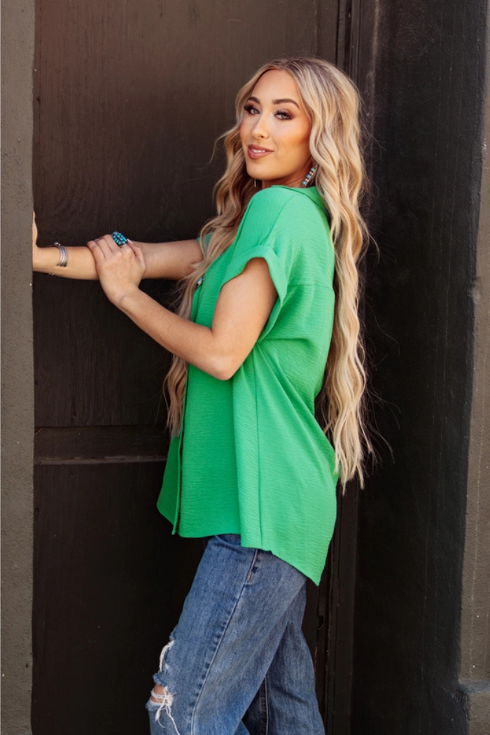 Woman wearing a Pleated button woven top in green with lightweight breathable fabric and blue jeans against a dark background