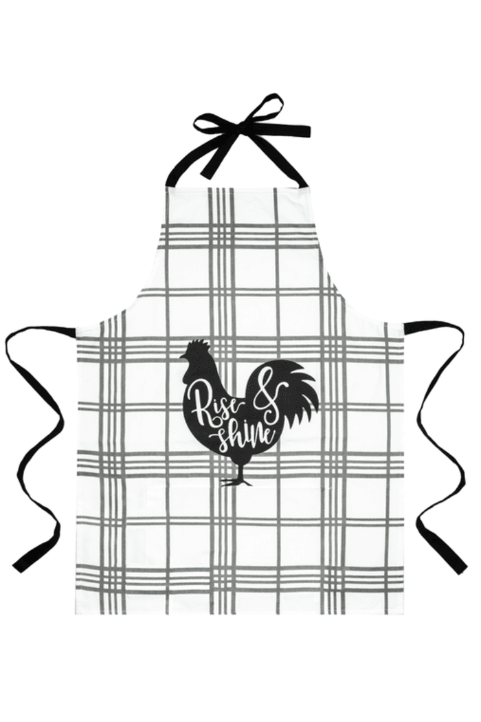  A black silhouette of a rooster is centered on the apron, with the words "Rise & Shine" written in a cursive font over the rooster's body. The apron has black ties at the neck and waist. 