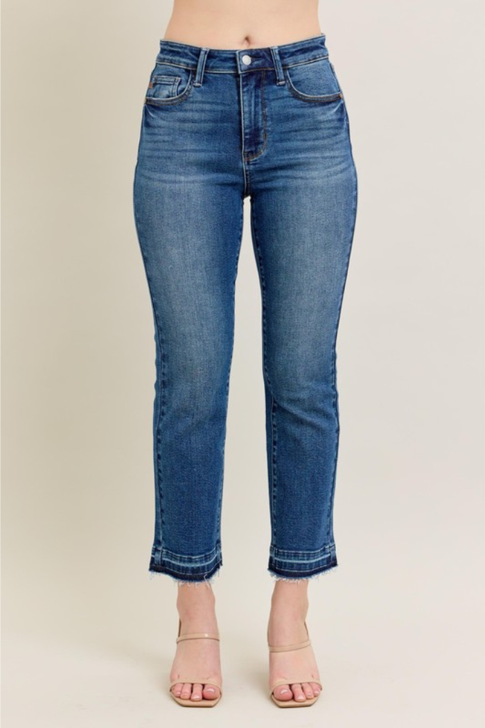 The image shows a pair of Judy Blue Vintage Wash Release Hem Jeans on a model. These jeans are characterized by a vintage wash and a released hem, giving them a slightly frayed and casual look. The jeans are a classic blue denim color and appear to be a mid-rise style. They are paired with nude heels, which help to elongate the legs and keep the focus on the jeans.