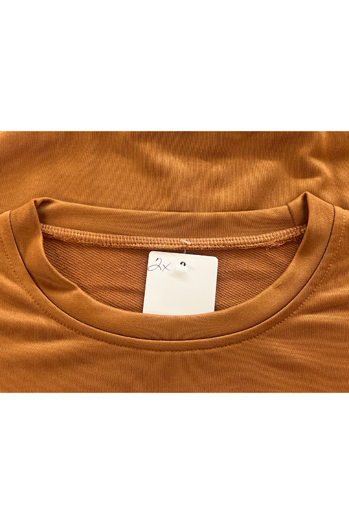 A close-up view of a brown-colored, top with a white tag displaying '2x' visible near the collar.