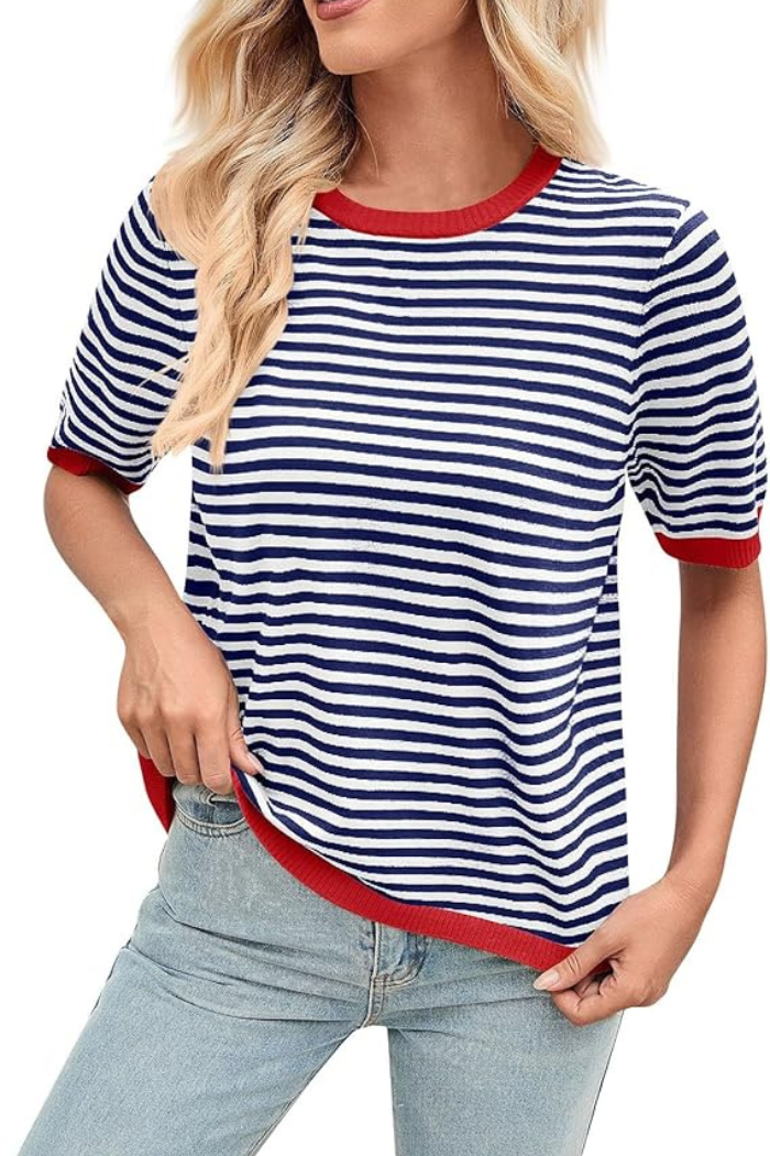 A woman wearing a navy blue and white striped t-shirt with red trim on the collar, sleeves, and hem, paired with light blue jeans.