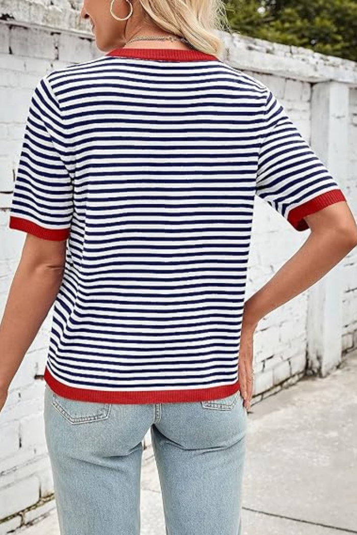 Back view of a person wearing a navy and white striped short-sleeve knit top with red trim on the collar, sleeves, and hem, paired with light wash jeans.