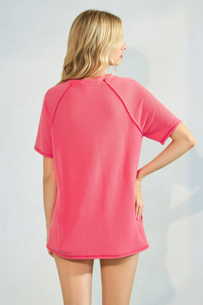 A woman from behind wearing a short-sleeved, ribbed, bright coral top and shorts.