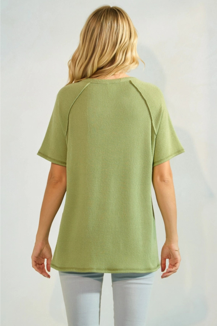 Rear view of a blonde woman wearing a relaxed-fit, short-sleeved, green top and light jeans.