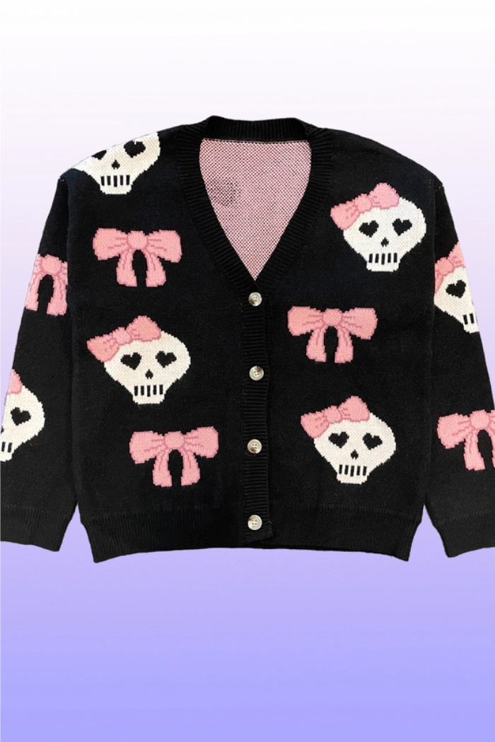 A black v-neck cardigan featuring a pattern of white skulls with pink bows on their heads and smaller pink bows scattered throughout, with button-front closure.