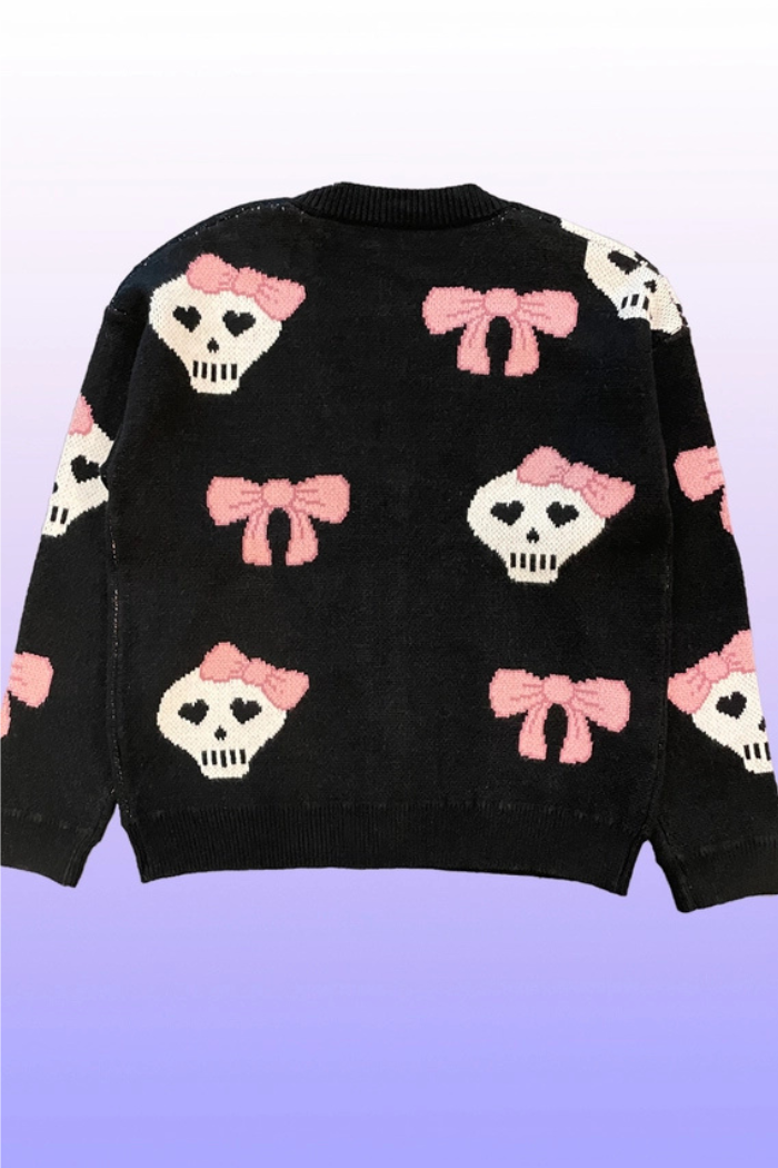 Back side of a black v-neck cardigan featuring a pattern of white skulls with pink bows on their heads and smaller pink bows scattered throughout.