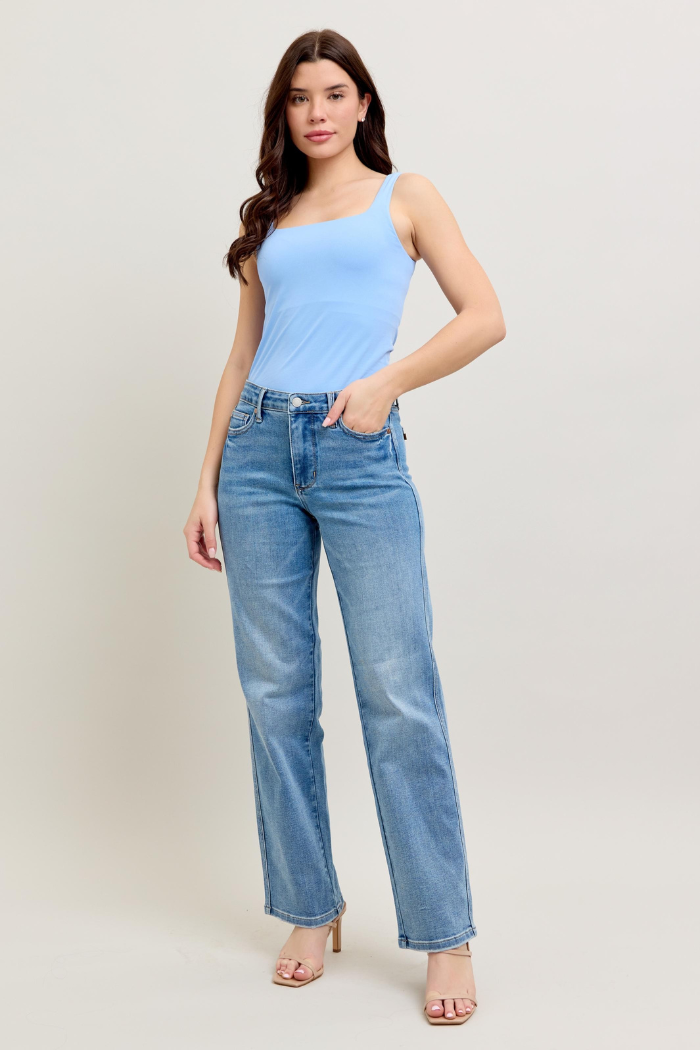 Woman wearing a light blue tank top and jeans on a plain background.
