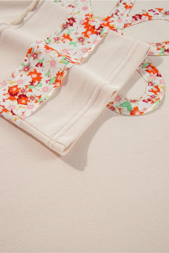 A close-up of a cream-colored garment featuring a colorful floral print design with visible, exposed seams and decorative stitching in cuff area.
