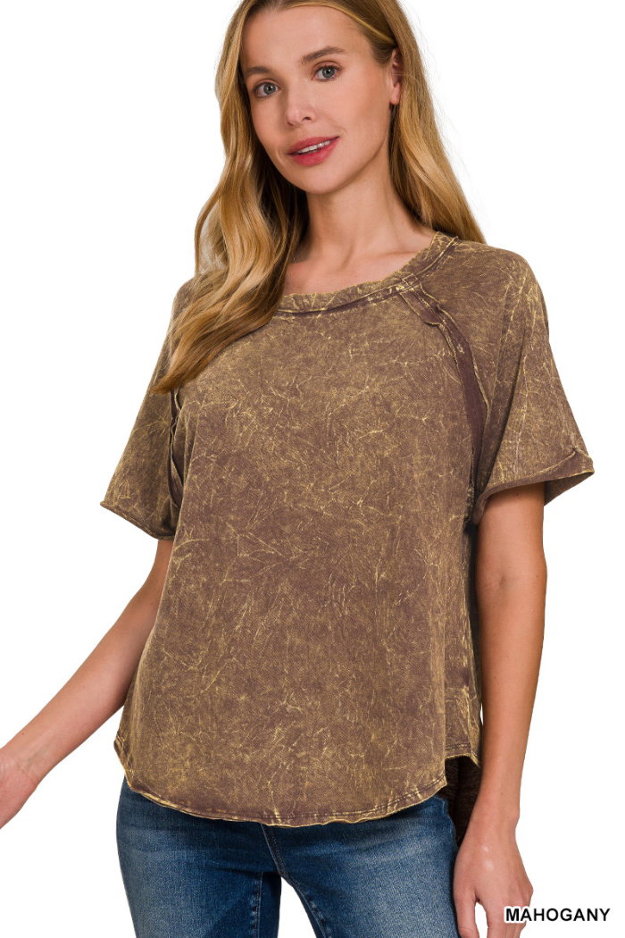 A woman wearing a mahogany-colored, acid-washed short-sleeved top with a round neckline and visible seams. The text "MAHOGANY" is present in the lower right corner of the image.