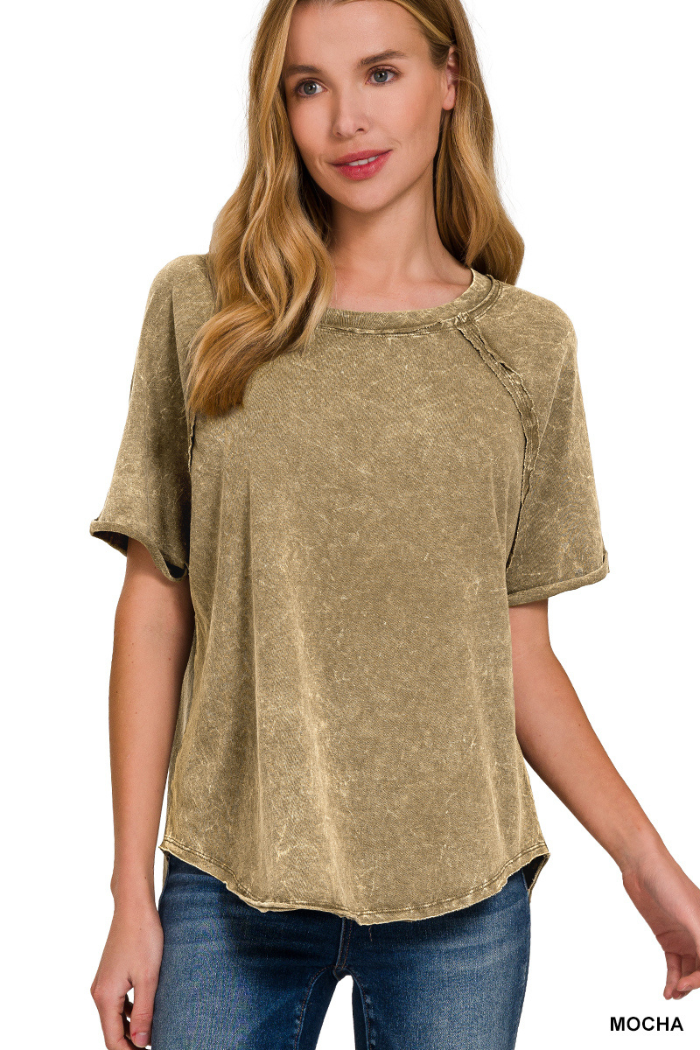 A woman wearing a mocha-colored, acid-washed short-sleeved top with raglan sleeves and a rounded hem, paired with blue jeans. The text "MOCHA" is visible in the bottom right corner of the image.