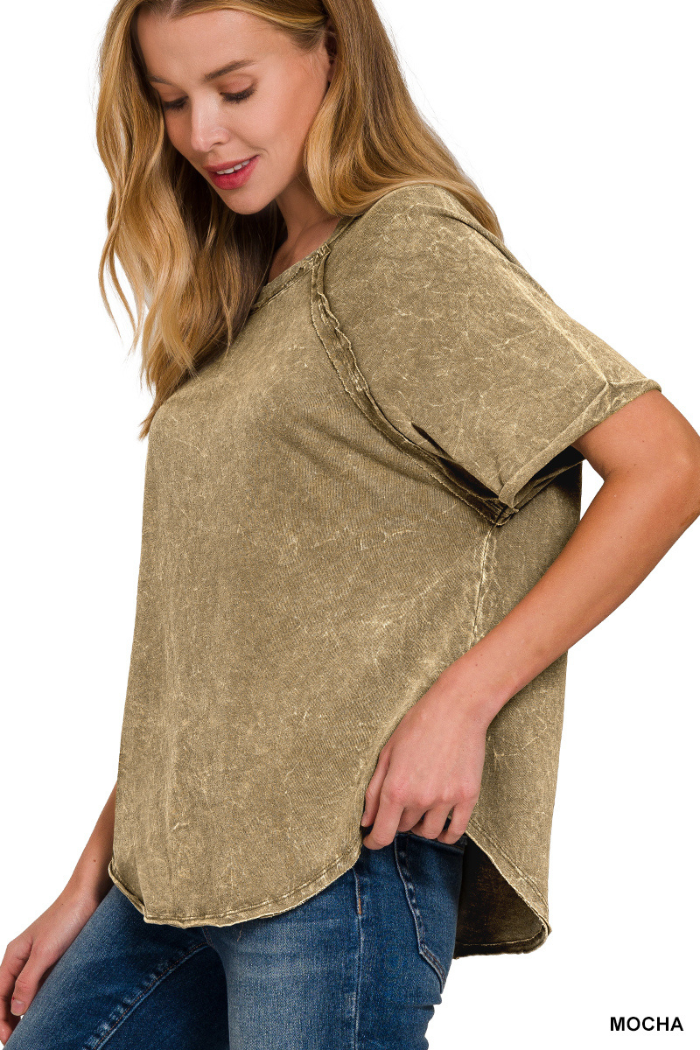 A woman wearing a mocha-colored, acid-washed short-sleeve top with visible seams and an arc hem, paired with blue jeans. The text "MOCHA" is visible in the bottom right corner.

