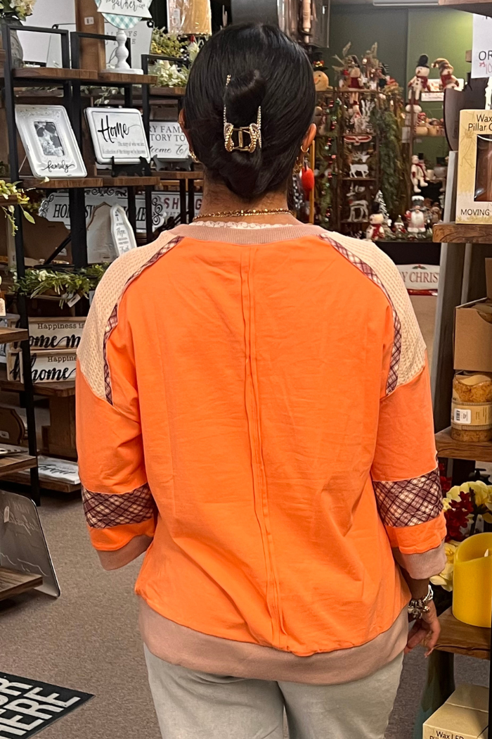 They are wearing an orange top with patterned sleeves and a lighter colored neckline back view.