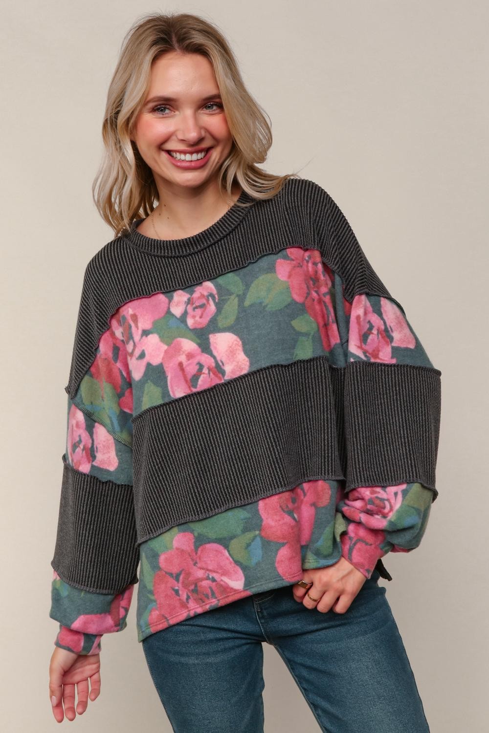 A smiling blonde woman wearing a long-sleeved, ribbed sweater with floral accents.