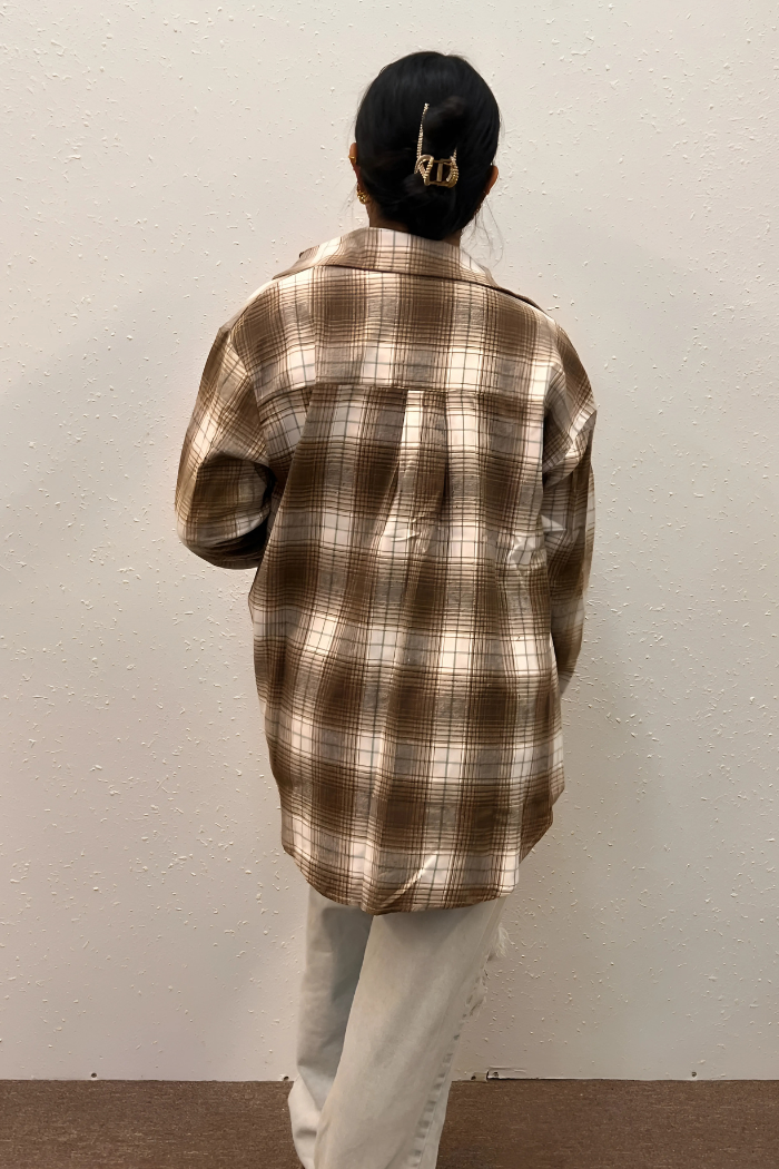 A person wearing a brown and white plaid flannel shirt and light-colored pants, viewed from behind. Their hair is styled up with a gold claw clip.