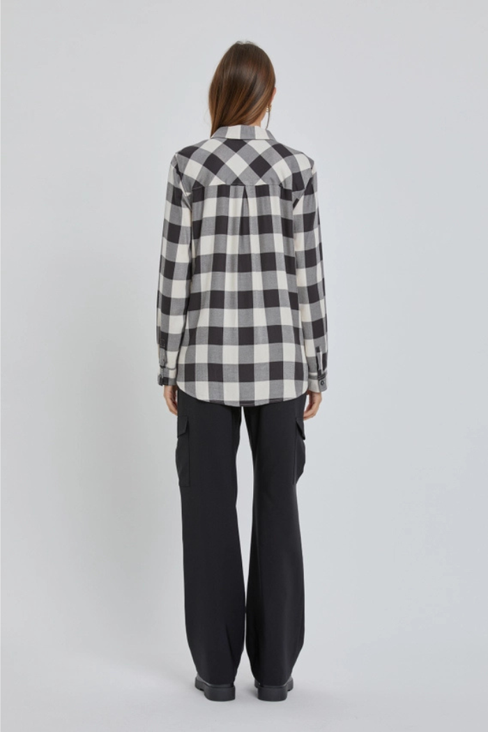 A person standing with their back to the viewer, wearing a black and white plaid flannel shirt and loose-fitting black wide-leg pants.