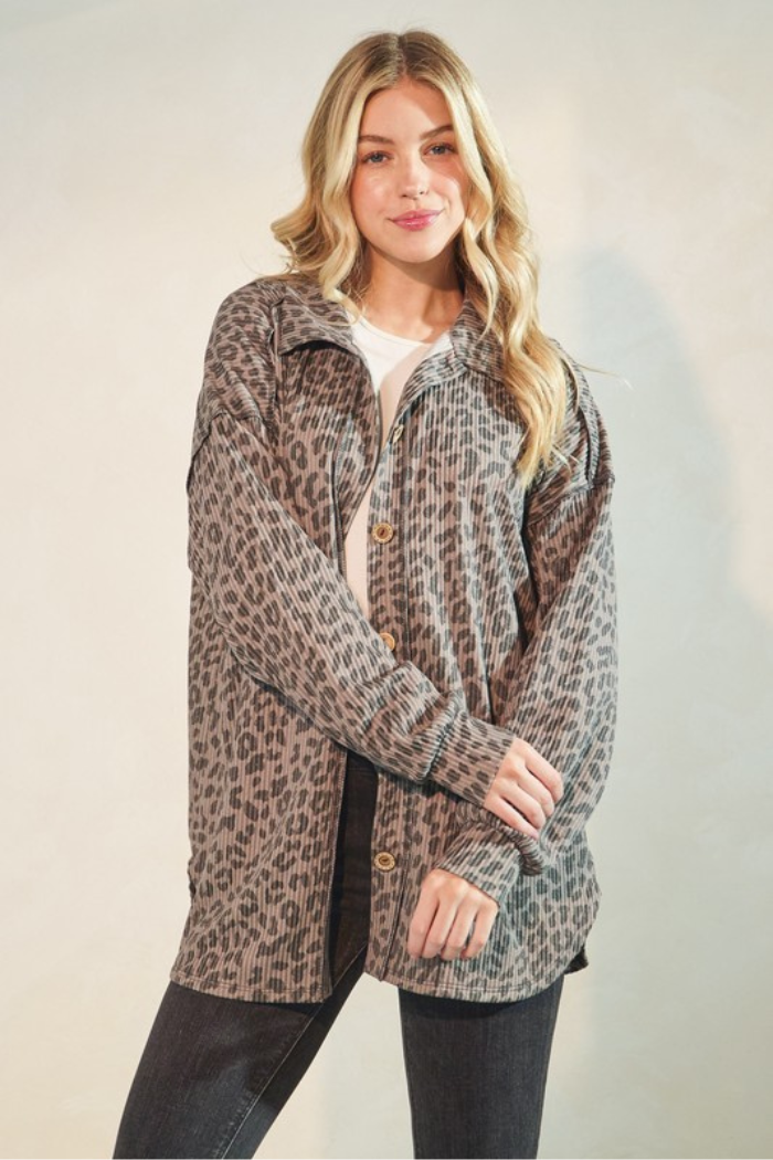 A young woman with long, wavy blonde hair smiles slightly while wearing a button-down shirt with an animal print pattern in shades of taupe and black. She is also wearing dark pants.