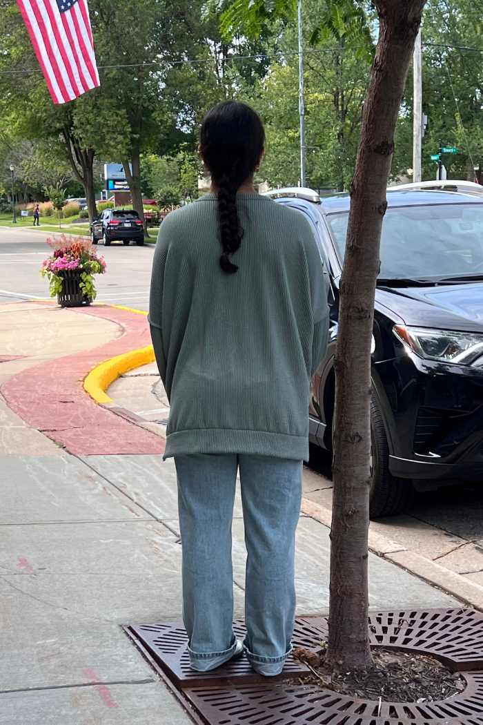 The person is wearing a loose-fitting, long-sleeved Olive oversized long sleeve top and light-wash jeans.