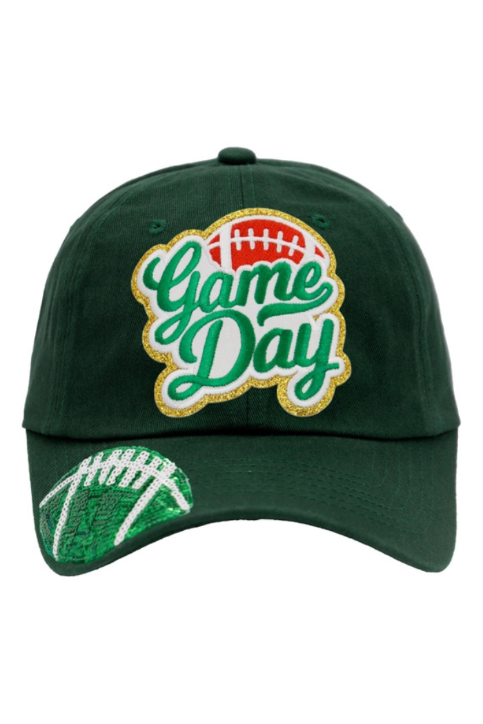 A dark green baseball cap featuring the embroidered text "Game Day" in a stylized font with gold glitter outlines and a small red football icon above the "Game" text. The brim of the cap is adorned with a large, sequined football design in green and white.