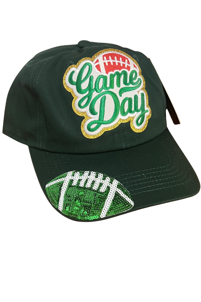 A side view of a green baseball cap featuring the embroidered text "Game Day" in a stylized font with gold glitter outlines and a small red football icon above the "Game" text. The brim of the cap is adorned with a large, sequined football design in green and white.