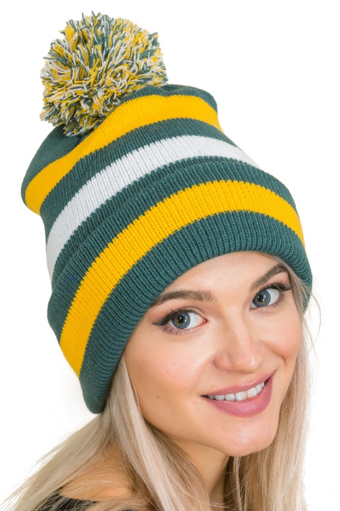 A woman wearing a knit beanie with green, white, and yellow stripes and a matching pom-pom on top, smiling at the camera. 